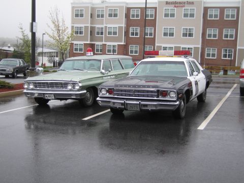 1991 Ford LTD Crown Victoria - green station wagon and a 1975 Plymouth police sedan parked side by side on wet pavement outside a Residence Inn.