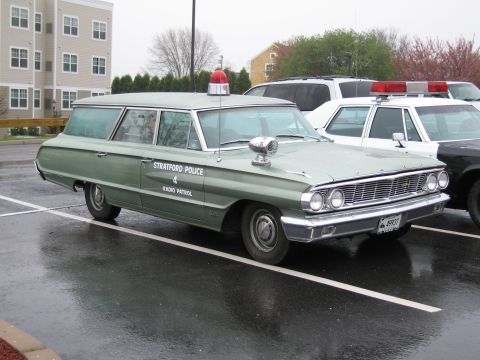 1991 Ford LTD Crown Victoria - green Ford station wagon lettered Stratford Police Radio Patrol with rooftop beacon parked on wet pavement.