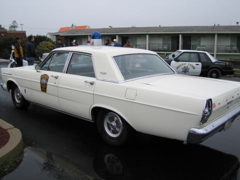 1991 Ford LTD Crown Victoria - white Ford State Police four-door sedan with a single blue roof beacon viewed from the rear in a wet lot.