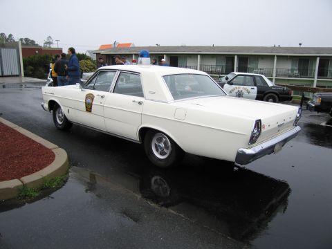 1991 Ford LTD Crown Victoria - white Ford State Police four-door sedan with a blue roof beacon parked on wet pavement outside a motel.