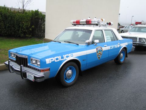 1991 Ford LTD Crown Victoria - blue-and-white NYPD Police Dodge sedan with blue wheels and red-and-white rooftop lights parked on pavement.