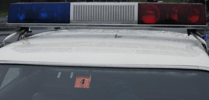 Police light bar with blue and red lights mounted on a white car roof. Orange sticker with a '4' is on the windshield