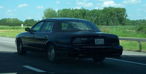 2001 Ford Crown Victoria - This black 2001 Ford Crown Victoria is seen driving on a highway, captured from a rear three-quarter perspective.