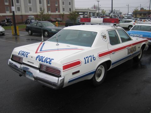 1991 Ford LTD Crown Victoria - white State Police sedan marked '1776' with red, white and blue stripes sits in a rainy lot among other classic patrol cars.