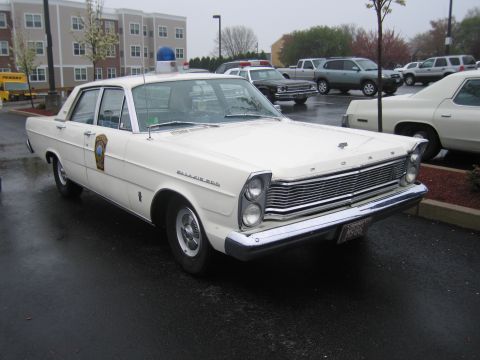 1991 Ford LTD Crown Victoria - white Ford Galaxie 500 State Police sedan with a single roof beacon parked on a wet lot in front of an apartment building.