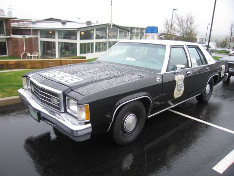 1991 Ford LTD Crown Victoria - black-and-white Ford LTD police sedan numbered 45 with 'POLICE' on the hood and a door shield parked on a wet lot.