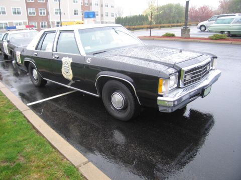 1991 Ford LTD Crown Victoria - black-and-white Ford LTD police sedan marked 45 with a door shield emblem parked on a wet lot among other patrol cars.