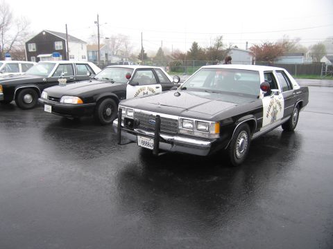 1991 Ford LTD Crown Victoria - black-and-white California Highway Patrol Ford LTD Crown Victoria with front push bar parked on a wet lot among other patrol cars.