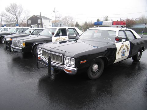 1991 Ford LTD Crown Victoria - black-and-white California Highway Patrol Dodge sedan with front push bar and roof lightbar parked among classic patrol cars on a wet lot.