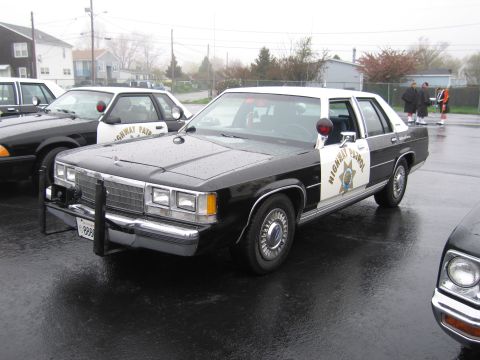 1991 Ford LTD Crown Victoria - black-and-white California Highway Patrol Ford LTD Crown Victoria with front push bar parked on a wet lot, other patrol cars nearby.