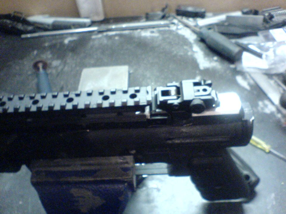 Close-up of a firearm sight on a Picatinny rail, secured in a vise on a workbench.