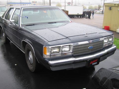 1991 Ford LTD Crown Victoria - dark blue Ford LTD Crown Victoria four-door sedan with DARE markings, parked on a wet lot showing its grille and quad headlights.