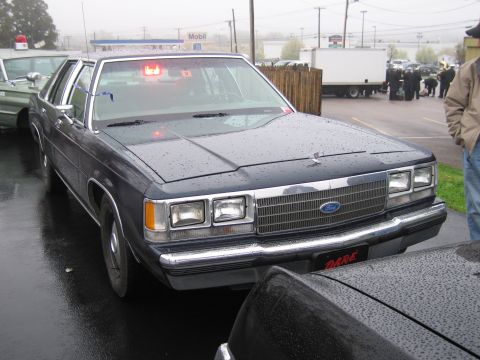 1991 Ford LTD Crown Victoria - dark Ford LTD Crown Victoria four-door sedan with a red dash light and DARE markings parked on a misty wet lot.