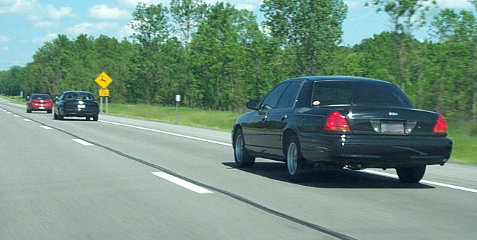 Black 2001 Ford Crown Victoria driving on a highway with another car behind it