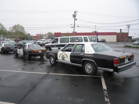 1991 Ford LTD Crown Victoria - Black-and-white California Highway Patrol cruisers, a Ford LTD sedan and a Fox-body Mustang, parked on a wet lot.