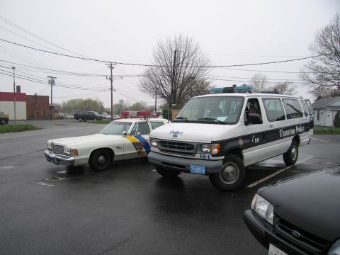 1991 Ford LTD Crown Victoria - white Dodge police sedan parked beside a white-and-blue Ford Econoline van marked Taunton Police on a gray wet lot.