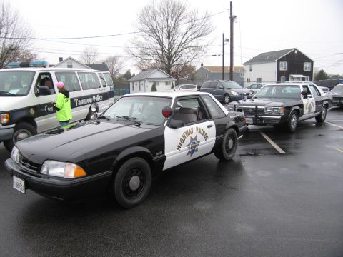 1991 Ford LTD Crown Victoria - black-and-white Fox-body Ford Mustang 5.0 California Highway Patrol cruiser parked among other cruisers on a wet lot.