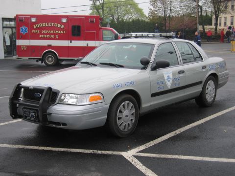 1991 Ford LTD Crown Victoria - silver Ford Crown Victoria marked Rhode Island State Police with a push bar and roof lightbar parked near a red ambulance.
