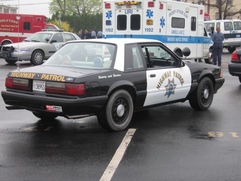 1991 Ford LTD Crown Victoria - black-and-white Fox-body Ford Mustang 5.0 California Highway Patrol cruiser shown from the rear near URI ambulances.
