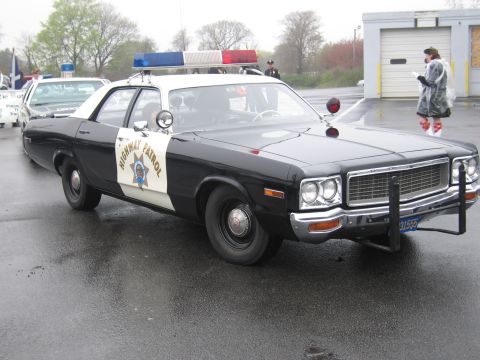 1991 Ford LTD Crown Victoria - black-and-white Dodge California Highway Patrol sedan with a push bar and roof lights parked on a wet lot.