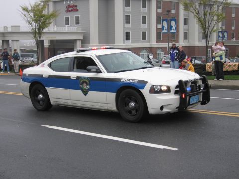 1991 Ford LTD Crown Victoria - White and blue Dodge Charger marked Police rolling down a wet street past spectators in a parade.