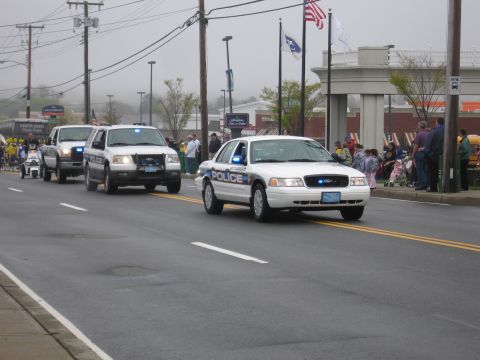 1991 Ford LTD Crown Victoria - white Ford Crown Victoria Police car leads a line of patrol vehicles down a foggy street lined with onlookers.