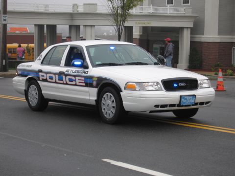 1991 Ford LTD Crown Victoria - White Attleboro Police Ford Crown Victoria supervisor cruiser with blue lights driving past a brick building.
