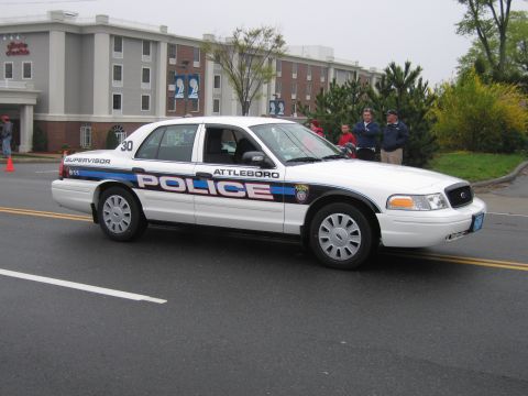 1991 Ford LTD Crown Victoria - White Attleboro Police supervisor Ford Crown Victoria with lights on rolls past a brick building and spectators.