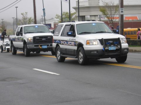 1991 Ford LTD Crown Victoria - White Attleboro Police Ford Expedition SUV and a marked pickup truck drive in a foggy parade past a school bus.