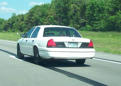2001 Ford Crown Victoria - Rear view of a white Ford Crown Victoria sedan traveling on a divided highway, shot from a following vehicle. It runs black steel wheels wi…