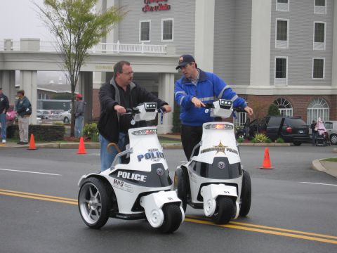 1991 Ford LTD Crown Victoria - Two men converse while riding white three-wheeled stand-up police mobility vehicles in front of a hotel.