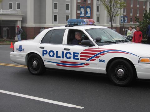 1991 Ford LTD Crown Victoria - White Metropolitan Police Crown Victoria with red-and-blue striping and number 950 driving on a parade street.