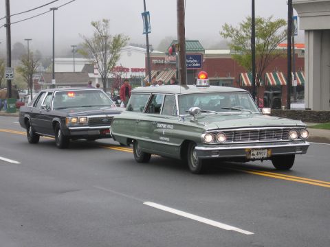 1991 Ford LTD Crown Victoria - Green vintage Ford Stratford Police station wagon with red dome light leads an older sedan in a parade.