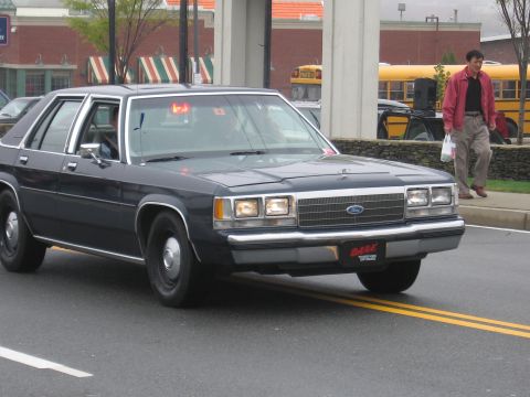 1991 Ford LTD Crown Victoria - Dark blue Ford LTD Crown Victoria sedan with a red DARE front plate driving past a man on a street.