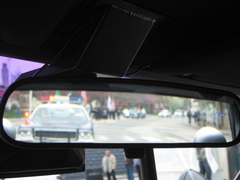 1991 Ford LTD Crown Victoria - car's rearview mirror reflects black-and-white police cruisers and a gathered crowd along a street behind the vehicle.