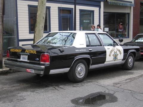 1991 Ford LTD Crown Victoria - Rear three-quarter view of a black-and-white Ford LTD Crown Victoria Highway Patrol sedan parked curbside outside a breakfast cafe.