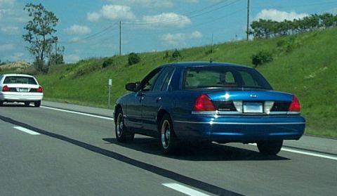 2001 Ford Crown Victoria - A blue 2001 Ford Crown Victoria sedan is seen from behind on a highway, with another white car ahead.