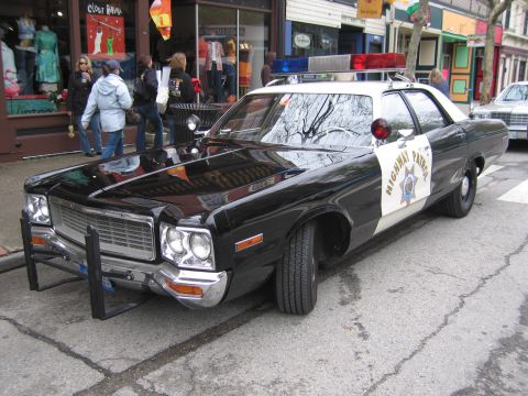 1991 Ford LTD Crown Victoria - Front three-quarter view of a black-and-white Highway Patrol sedan fitted with a front push bar, parked curbside among pedestrians.