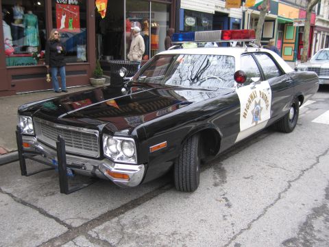 1991 Ford LTD Crown Victoria - black-and-white Highway Patrol sedan with a gold star-badge decal and front push bar parked along a storefront-lined street.