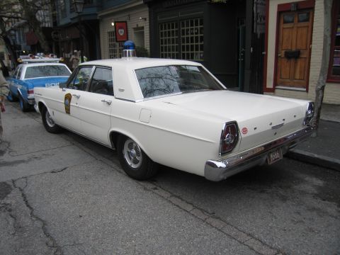 1991 Ford LTD Crown Victoria - Rear three-quarter view of a white 1960s Ford Galaxie police sedan with a single blue rooftop beacon parked on a street.