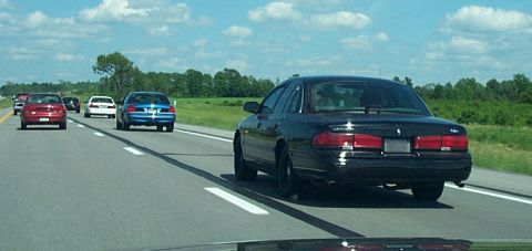 2001 Ford Crown Victoria - A black 2001 Ford Crown Victoria travels down the highway alongside other vehicles on a sunny day.