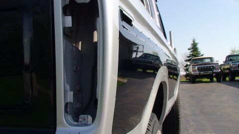 1979 Ford Bronco - Reflection of a Ford F-Series truck in the side panel of another similar truck, with two more trucks visible in the background.