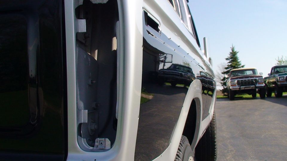 Black Ford F-Series truck side view, showing reflection of another truck and two other trucks parked in background