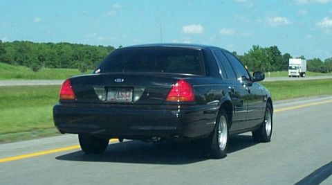 2001 Ford Crown Victoria - Rear view of a black 2001 Ford Crown Victoria on the highway under a clear sky.