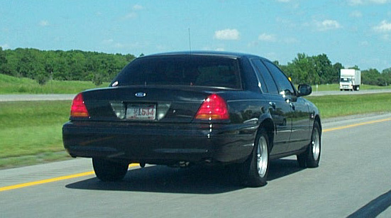 Black 2001 Ford Crown Victoria driving on highway, rear view. License plate visible