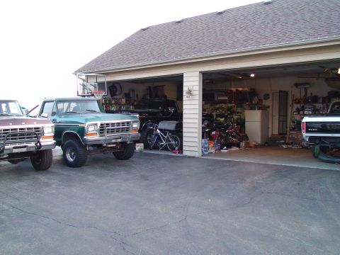 1979 Ford Bronco - Three pickup trucks are parked outside a garage. The green truck in the foreground is a 1979 Ford Bronco.