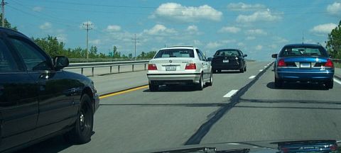 2001 Ford Crown Victoria - Multiple vehicles travel down a highway on a sunny day with scattered clouds.