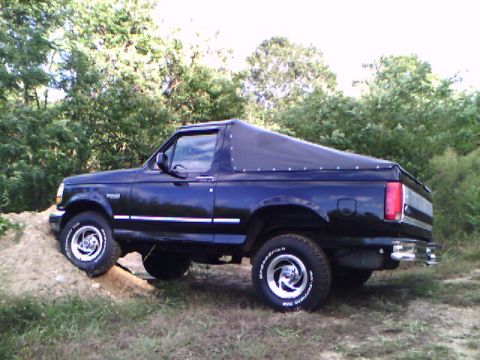 1995 Ford Bronco - This black 1995 Ford Bronco features a removable soft top and is shown navigating an off-road incline.