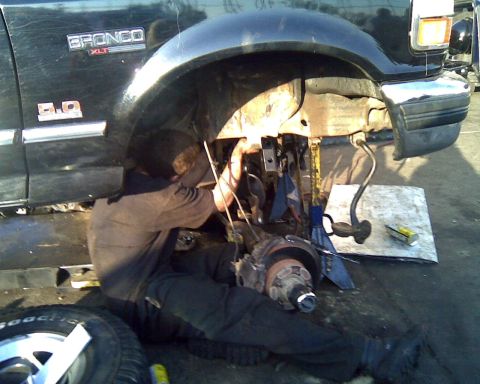 1995 Ford Bronco - A mechanic works on the suspension of a black 1995 Ford Bronco XLT, with the front passenger wheel removed.