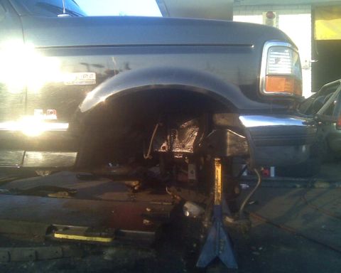 1995 Ford Bronco - Front fender and wheel well of a dark 1995 Ford Bronco undergoing repairs, supported by jack stands.